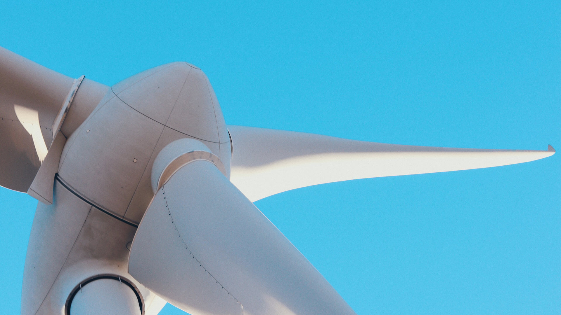 Close-up image of white wind turbine blades against a blue sky.