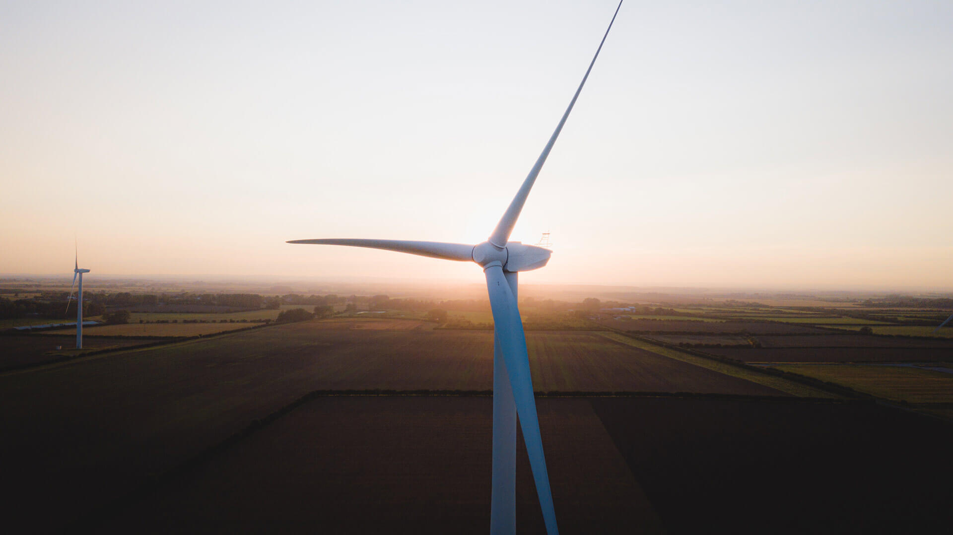 Close-up image of wind turbine blades against the sunrise over a farm field.
